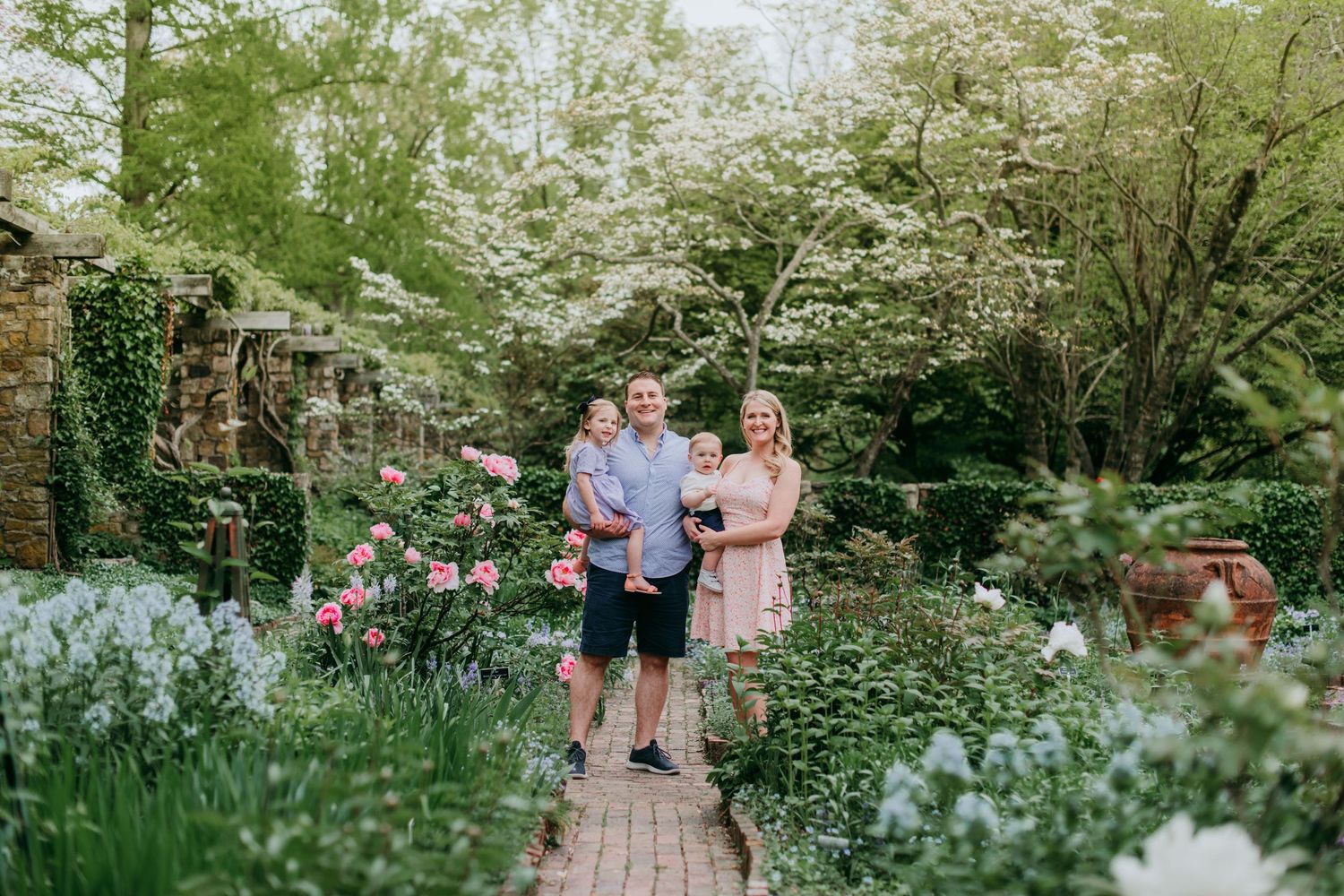A couple stands together on a garden path surrounded by blooming flowers and lush greenery on a spring day at Cross Estate Gardens in NJ.