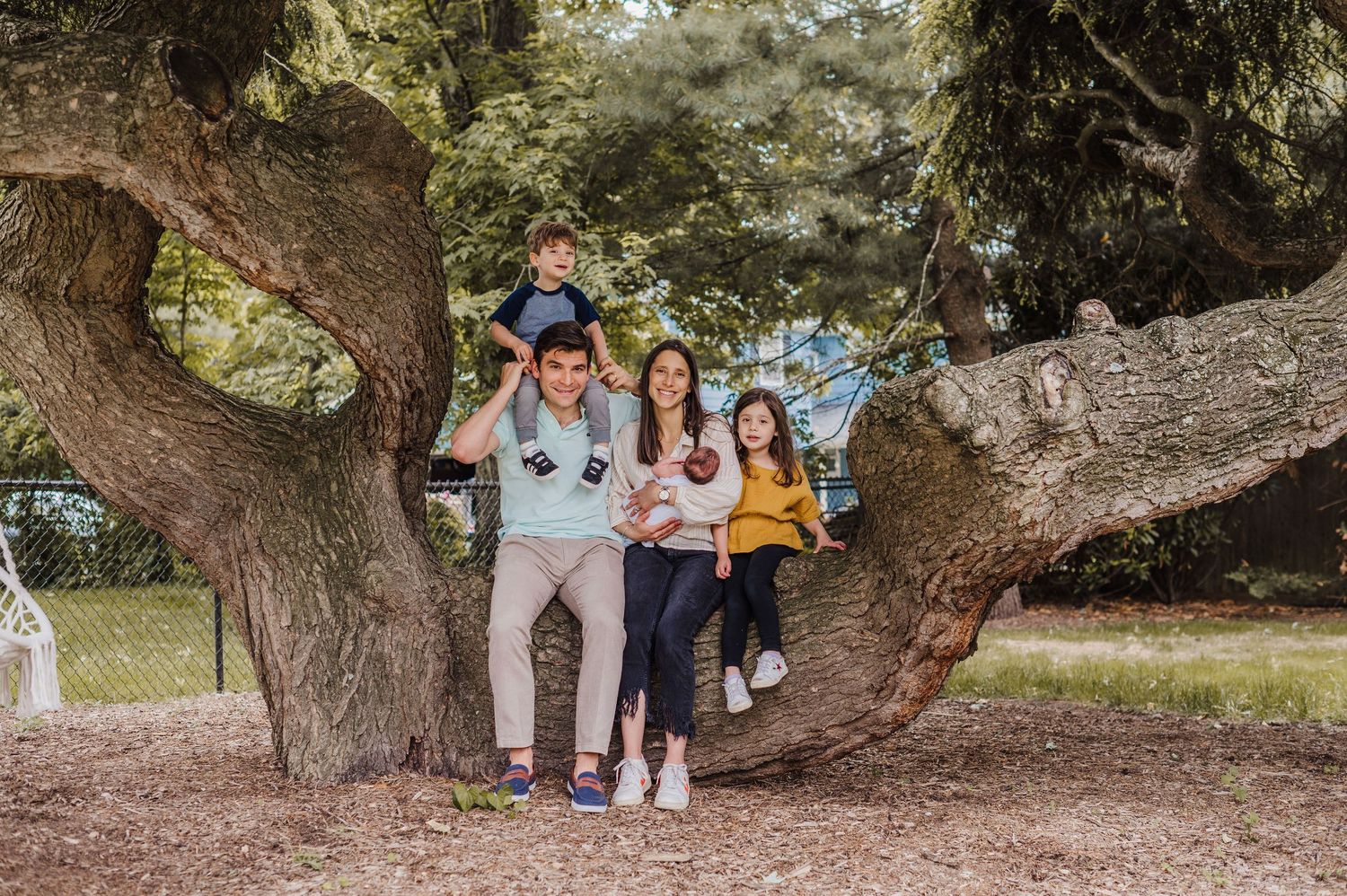 Three friends sharing a fun moment together while standing on a large twisted tree trunk in a park setting in Short Hills.