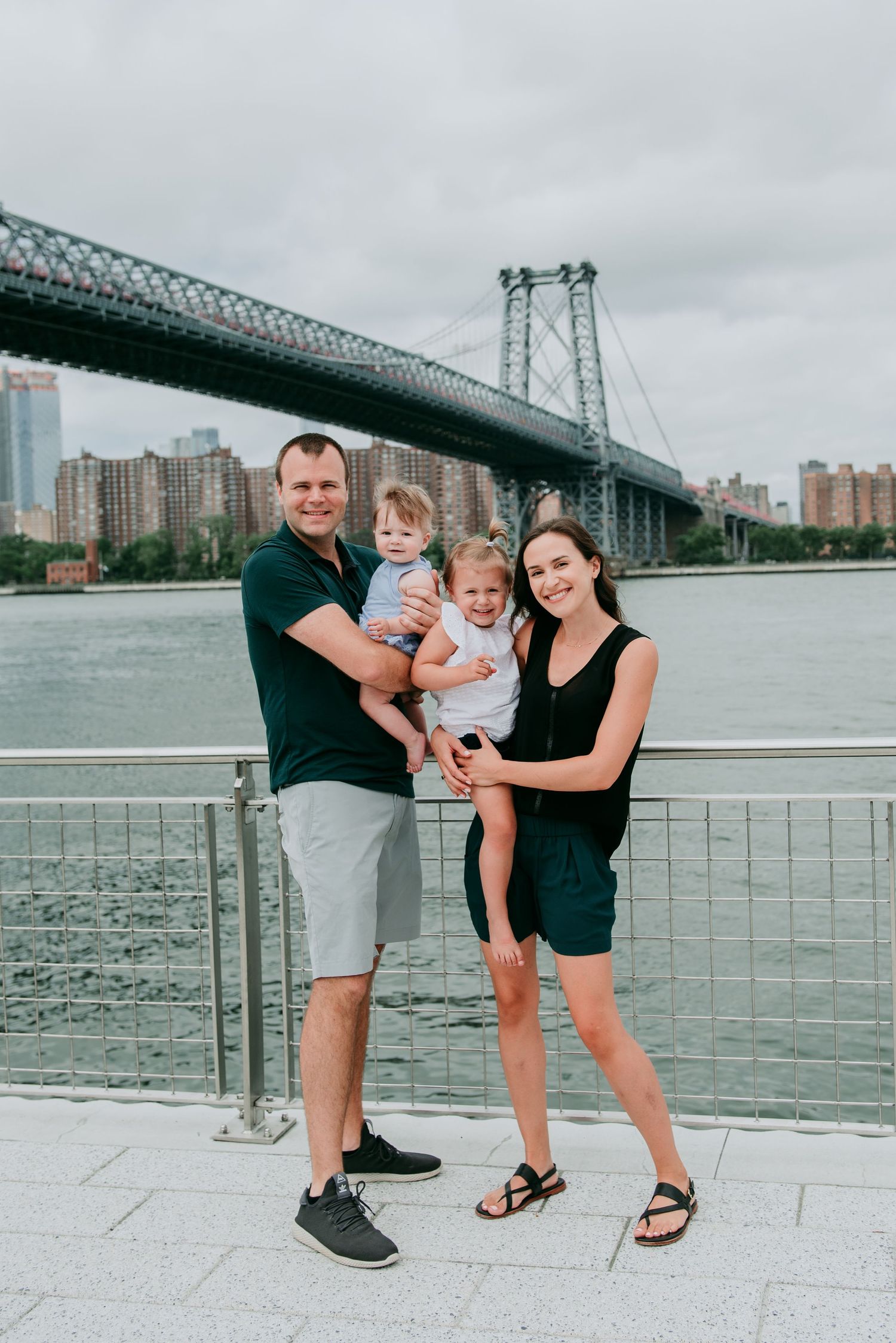 A family poses together at the waterfront with the Williamsburg Bridge in New York City visible in the background in Brooklyn.