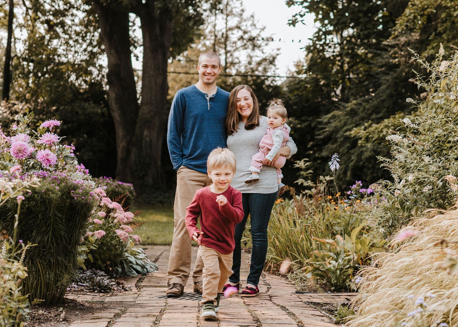 A family enjoying a sunny afternoon walk together on a garden path surrounded by flowering plants and trees in Montclair.