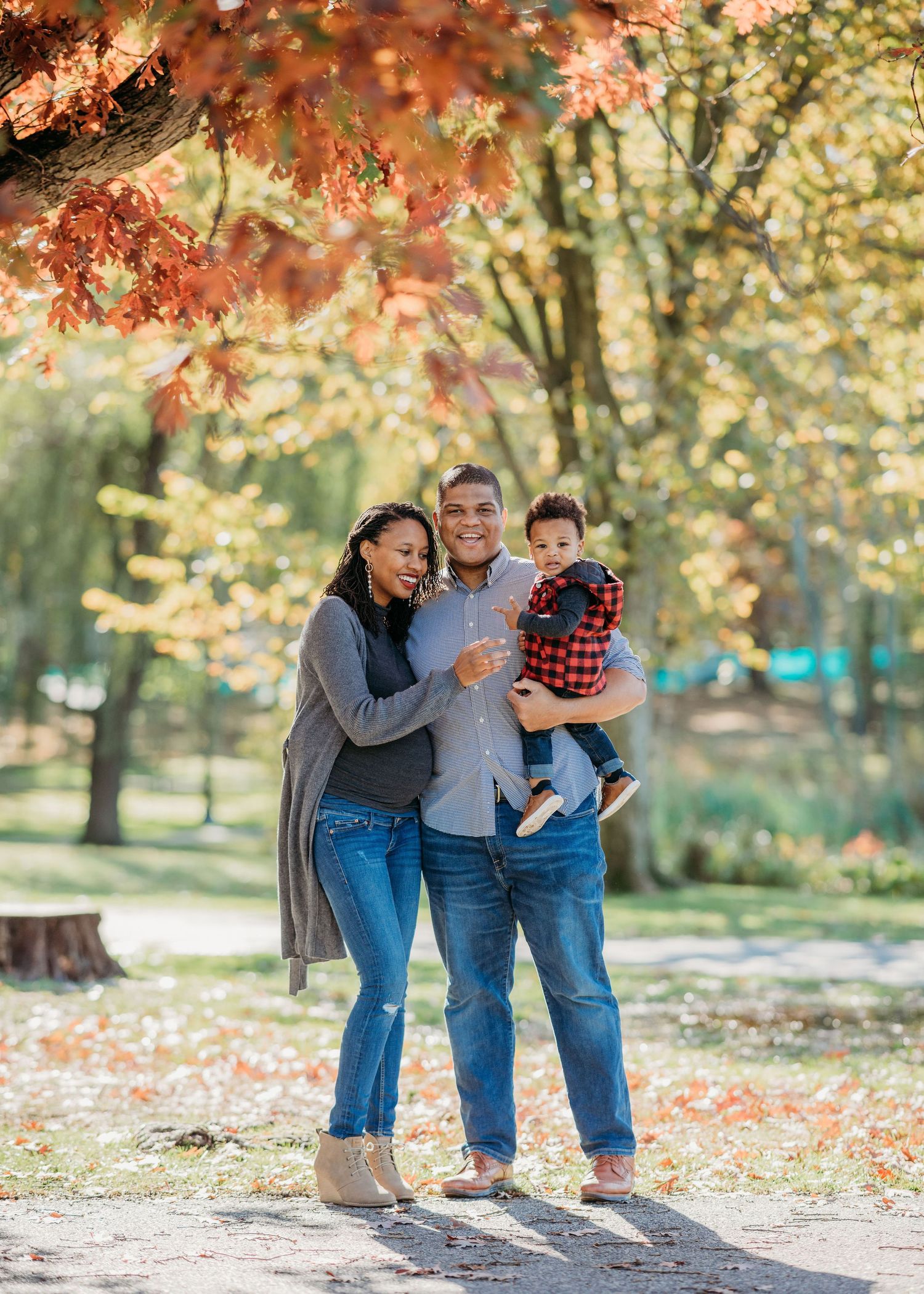 Three people enjoying a beautiful autumn day under colorful maple trees in a park with falling leaves.
