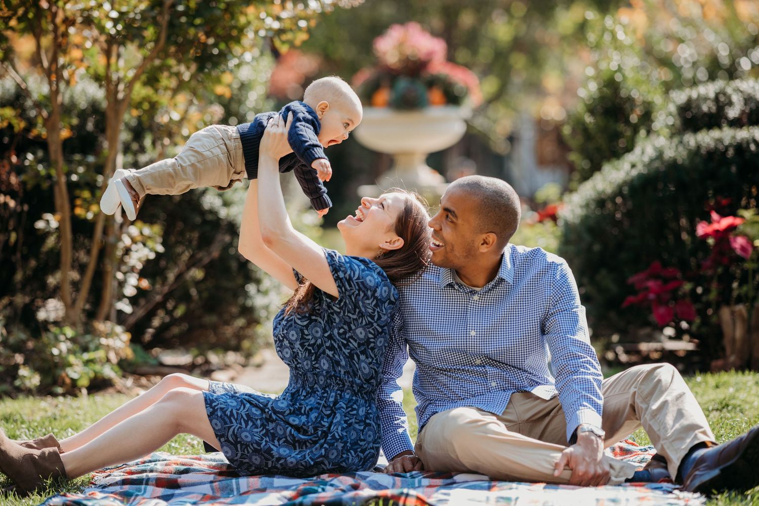 Family having a picnic in a garden setting while lifting a joyful baby in the air while sitting on a blanket at Freeman Gardens.