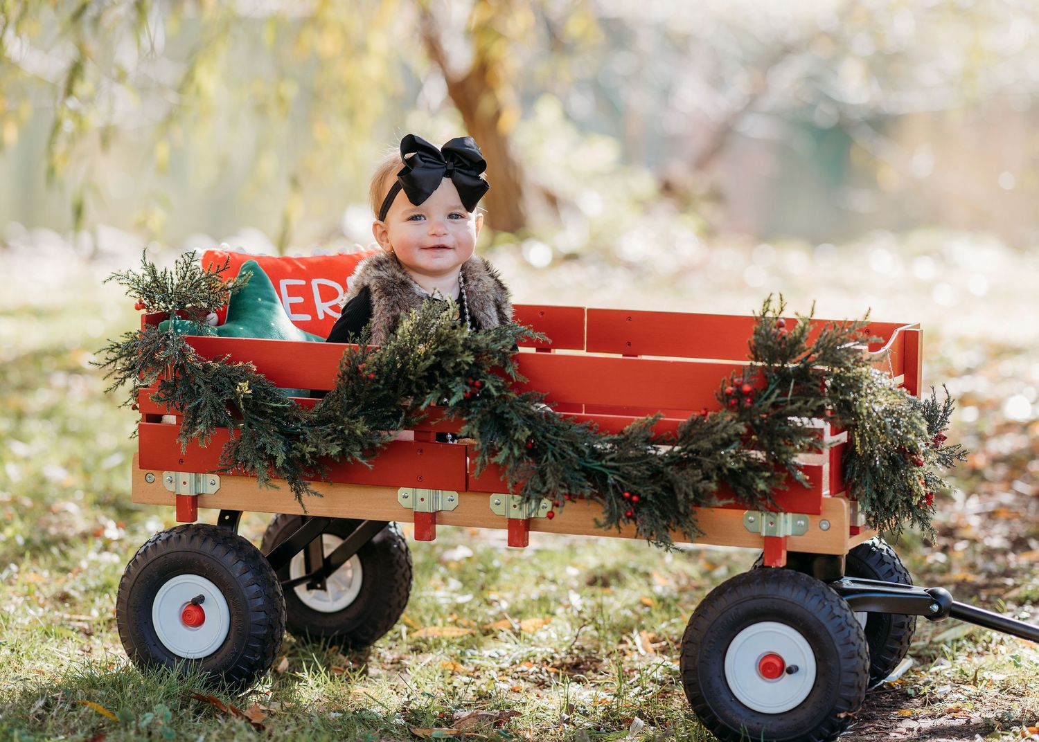 A red wooden wagon decorated with holiday greenery and garland sits in a sunny outdoor setting.