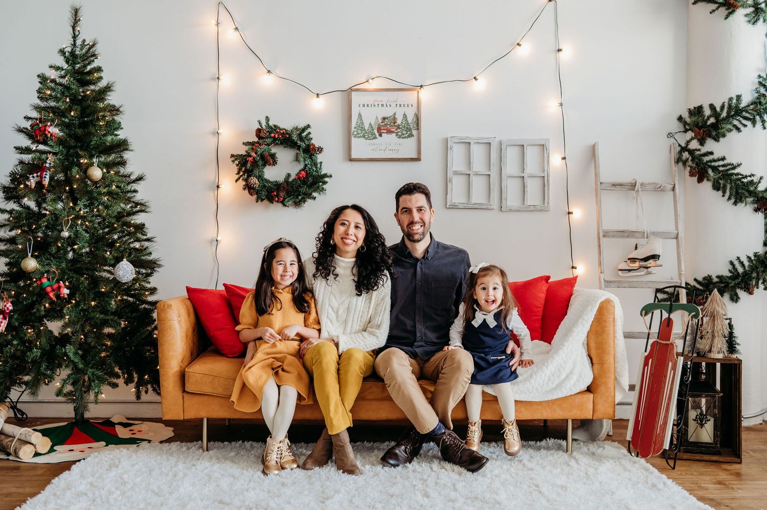 A family sits on a couch during Christmas with decorated trees, string lights and festive holiday decor in the studio.