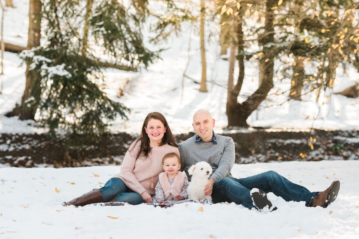 A family sits together in the snow with their white dog on a bright winter day in Nutley.