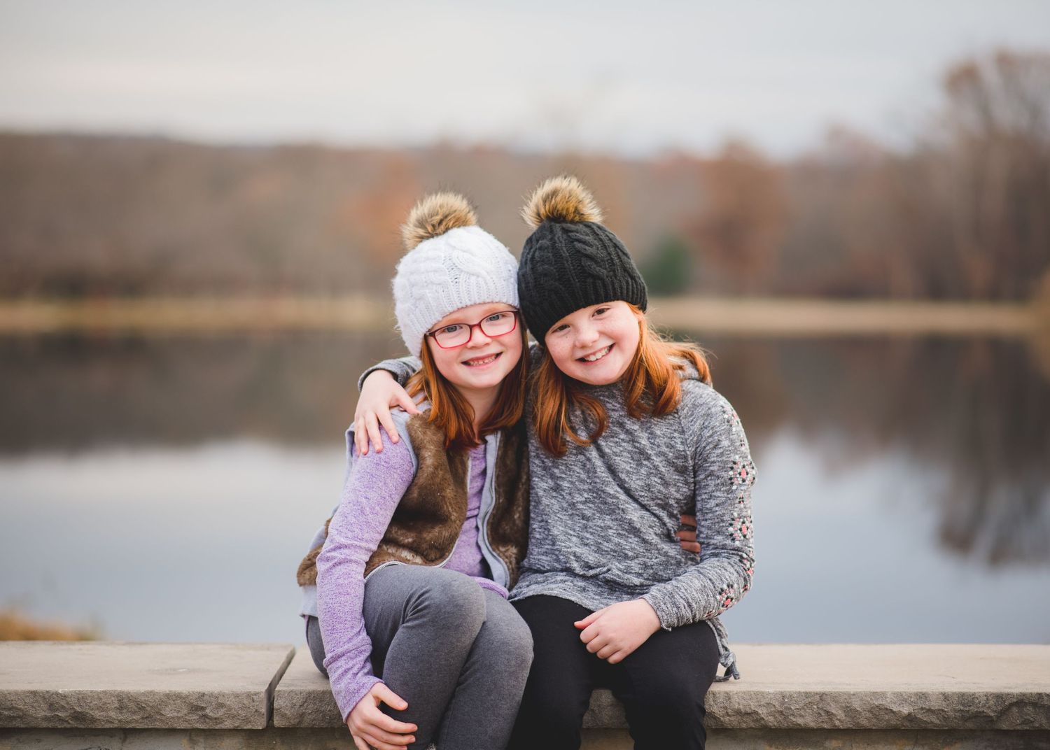 Two young friends wearing winter hats sit close together on a wooden dock by a peaceful lake at Horseshoe Lake in Succasunna, Roxbury.