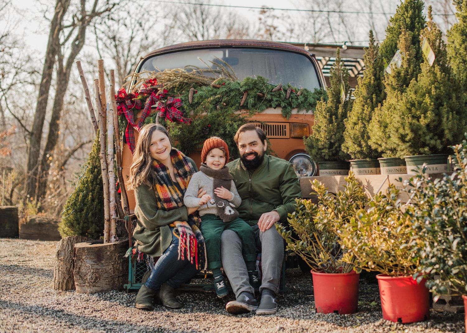 A family sits together on a bench surrounded by potted plants and Christmas decor in a garden setting in Totowa in front of a Volkswagen bus