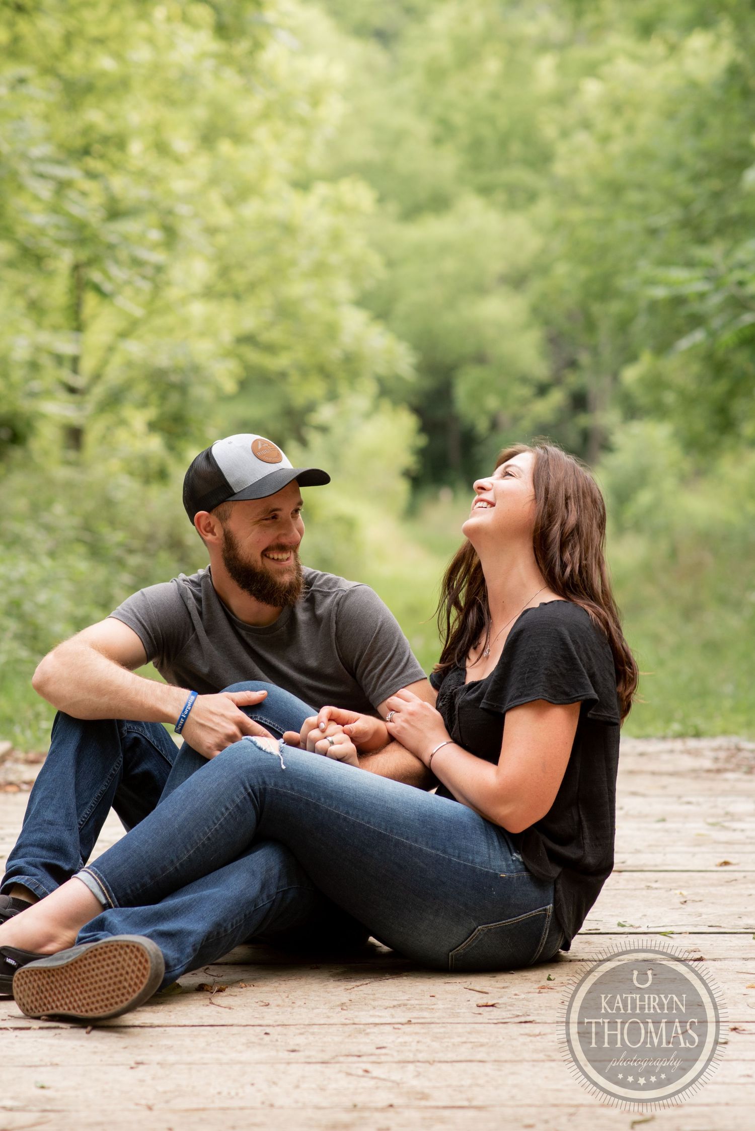 A couple shares a joyful moment while sitting on a wooden deck in nature.