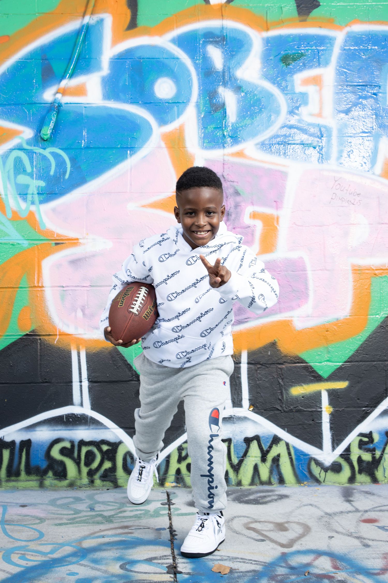 Young person holding football poses against colorful graffiti background.