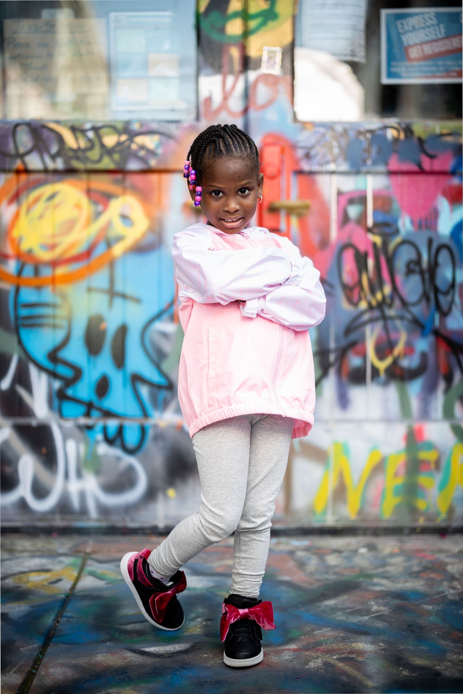Child in pink jacket strikes confident pose against graffiti wall.