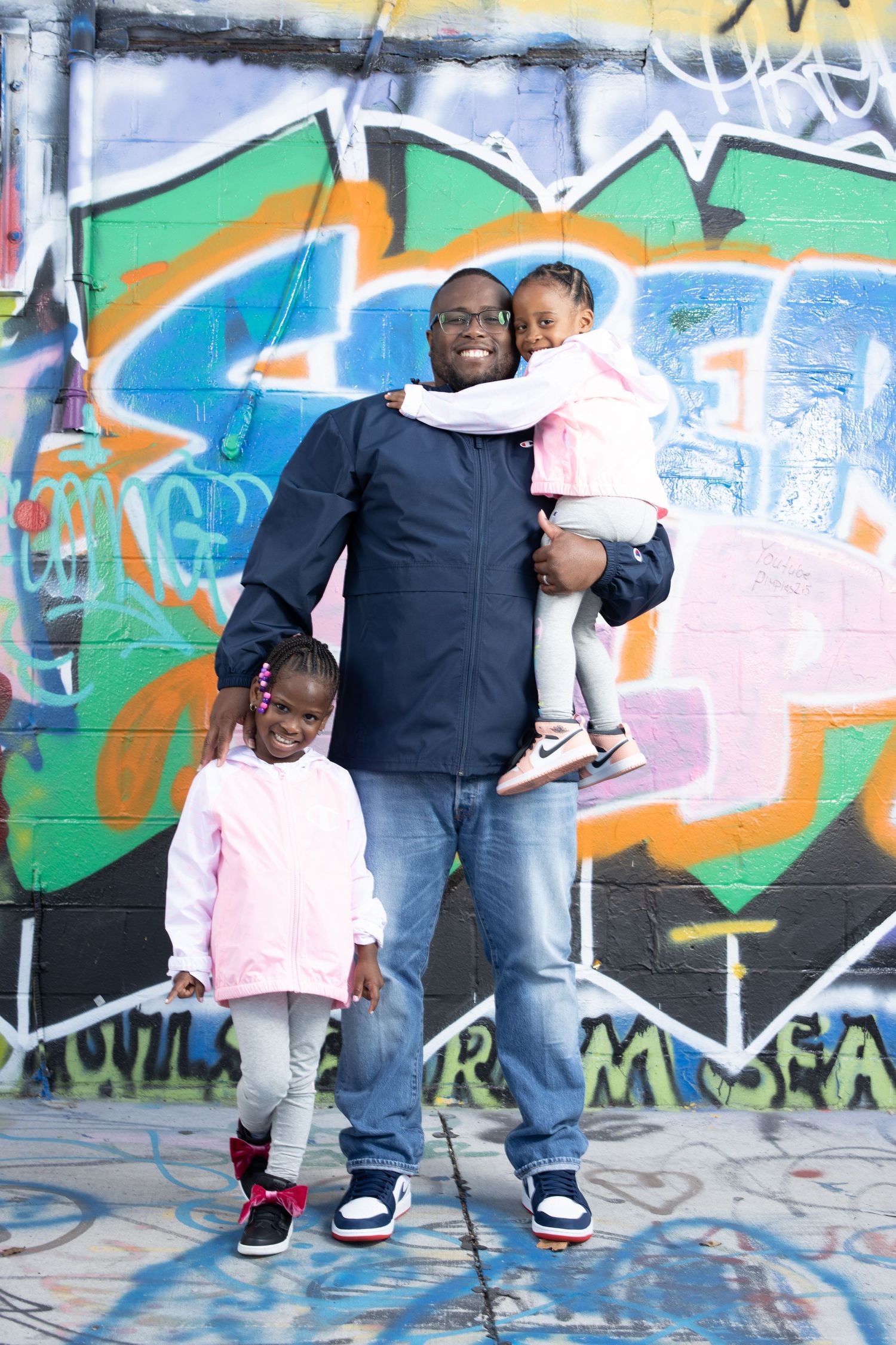 Parent with children posing against colorful graffiti wall.