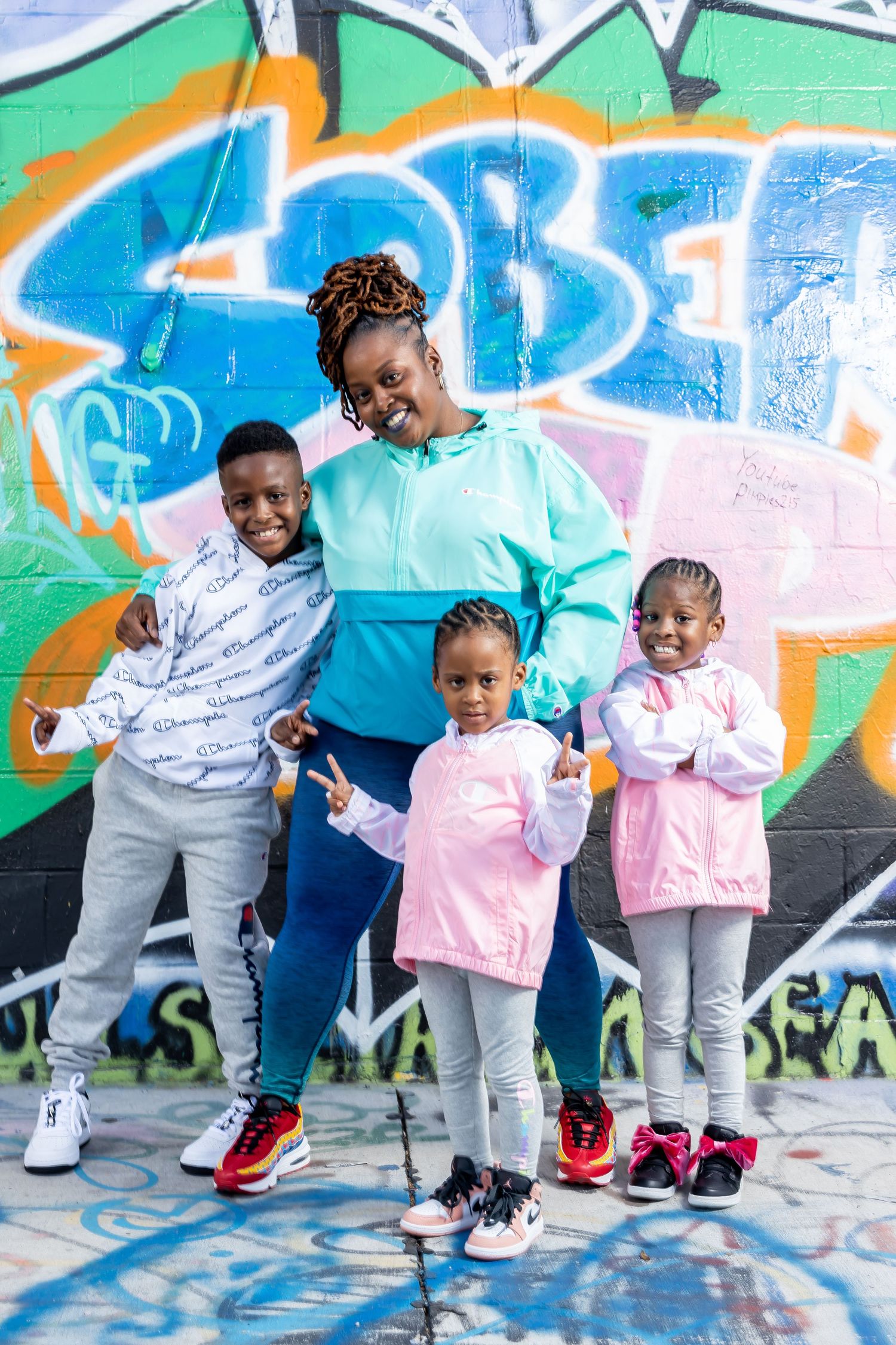 Family of four posing playfully against blue and green graffiti wall.