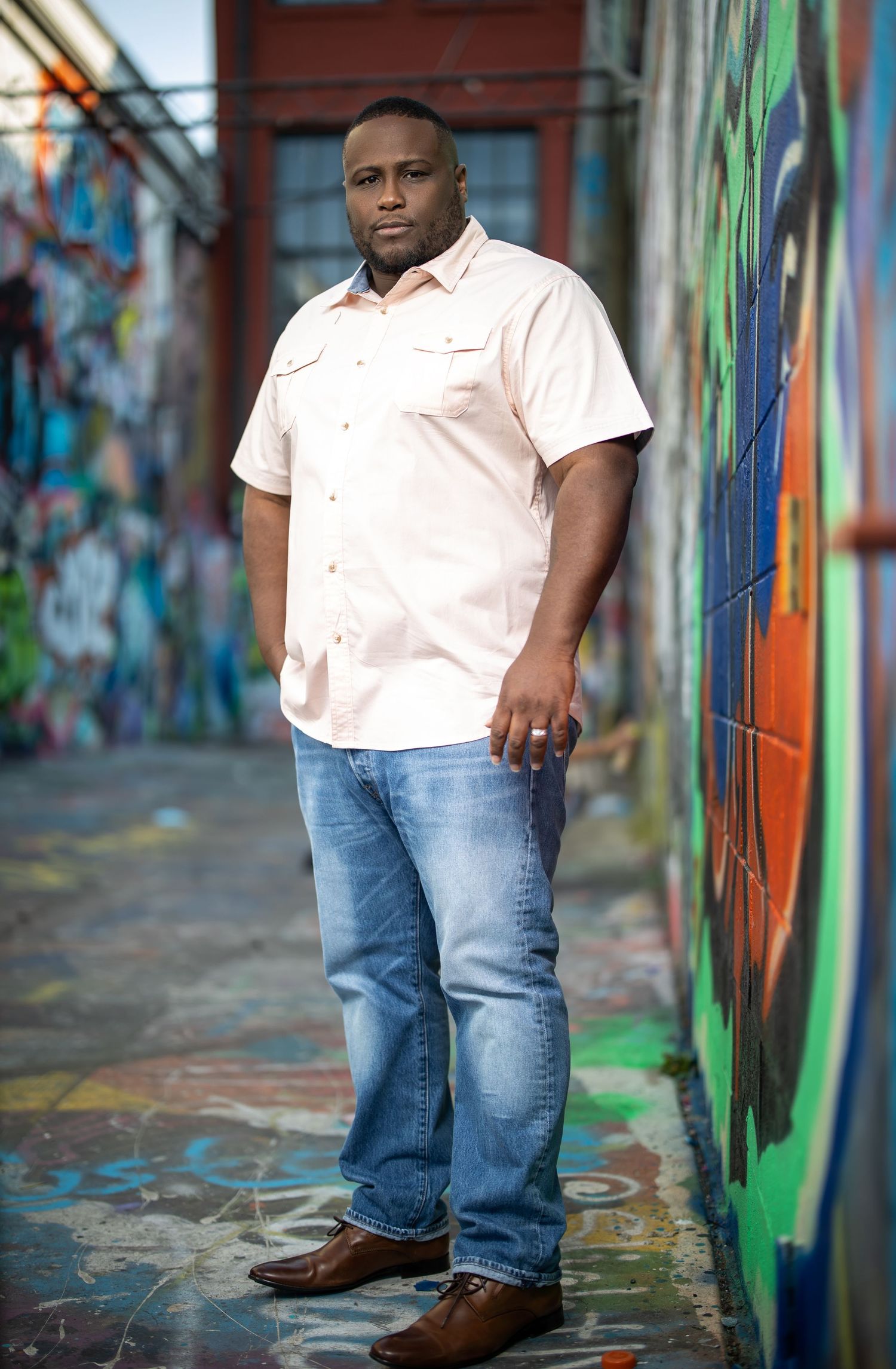 Person in white shirt and jeans stands confidently against colorful graffiti wall background.