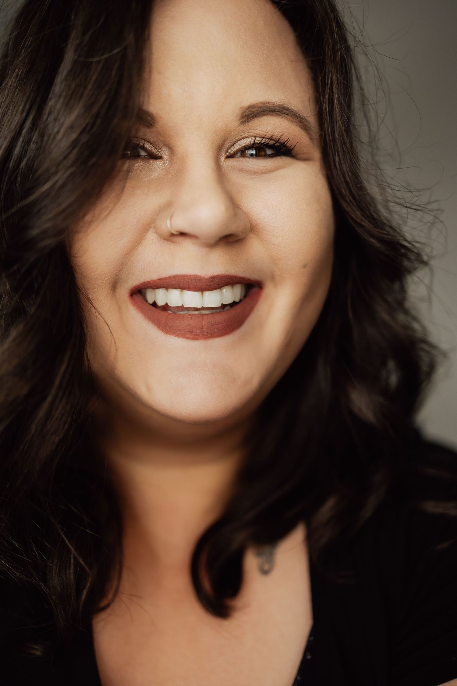Studio portrait with dark hair and joyful expression against grey backdrop.