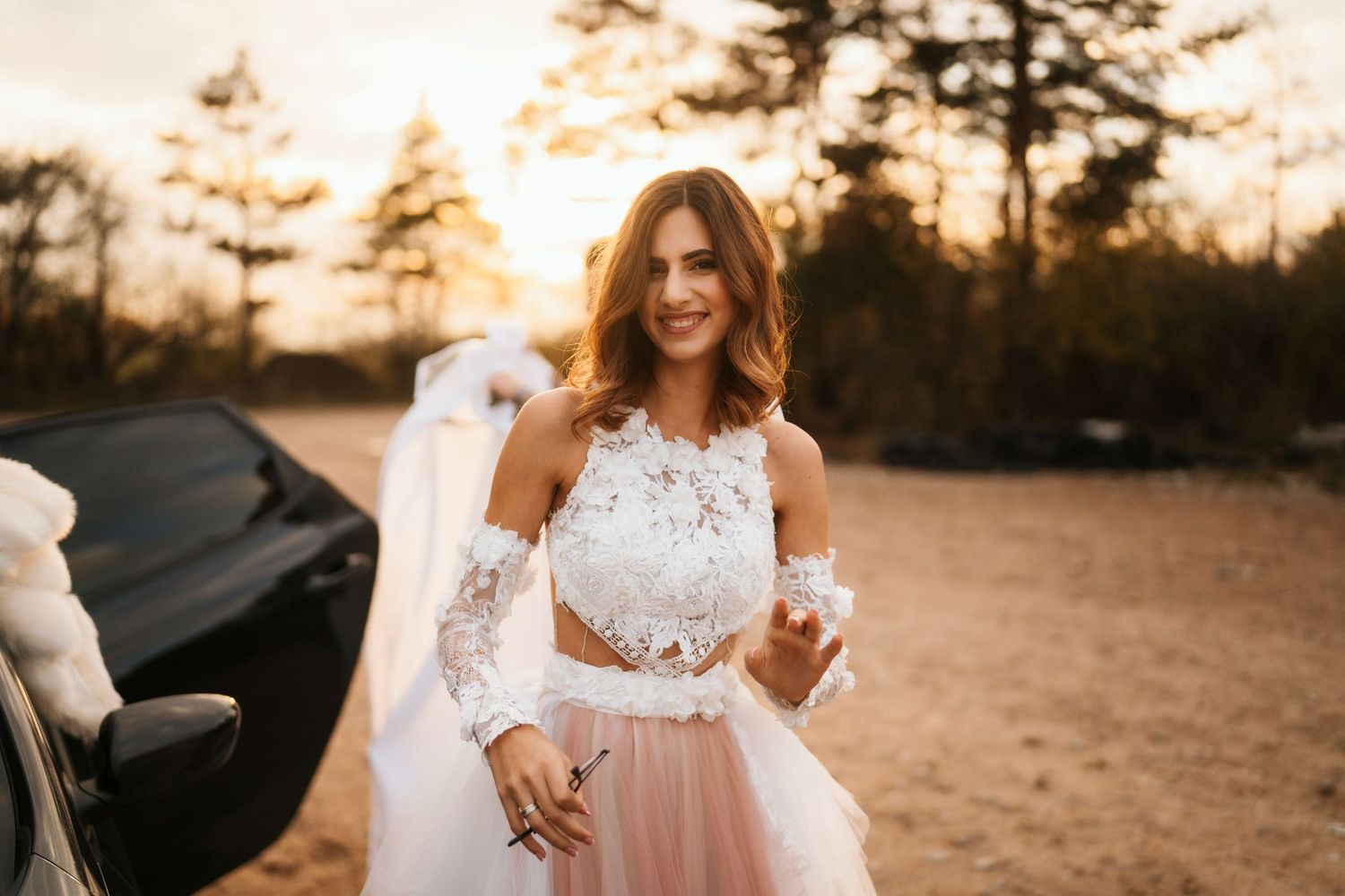 Ethereal wedding photo with lace dress against sunset in outdoor setting.