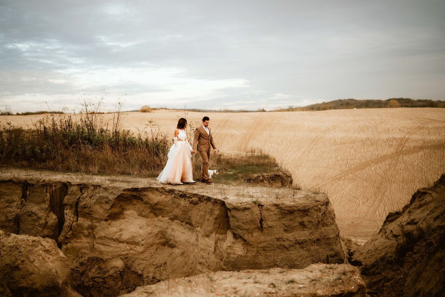 Wedding couple standing on dramatic cliff edge overlooking desert landscape.
