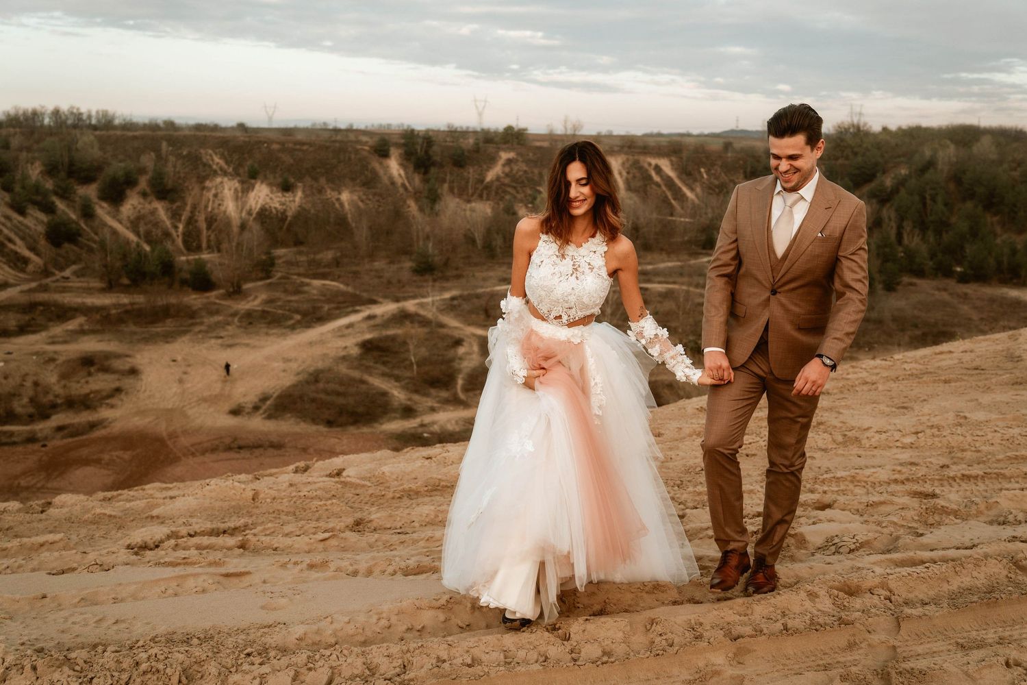 Wedding couple walking on rugged terrain with pink tulle dress and brown suit.