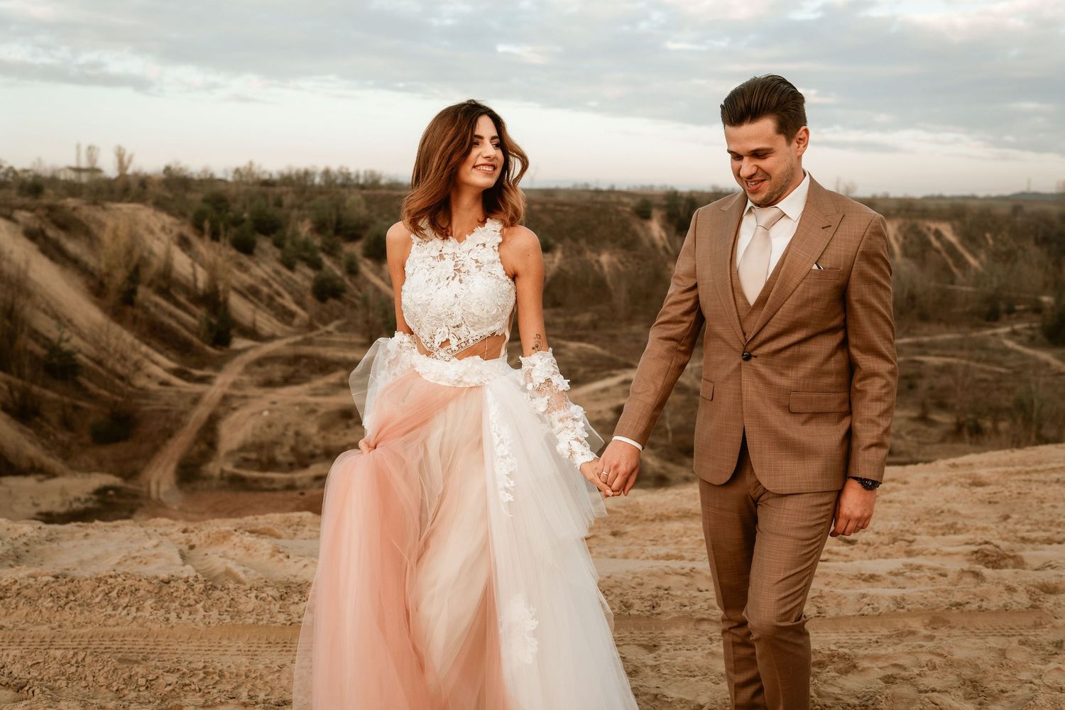 Romantic wedding photo on rocky terrain with pink tulle dress and brown suit.