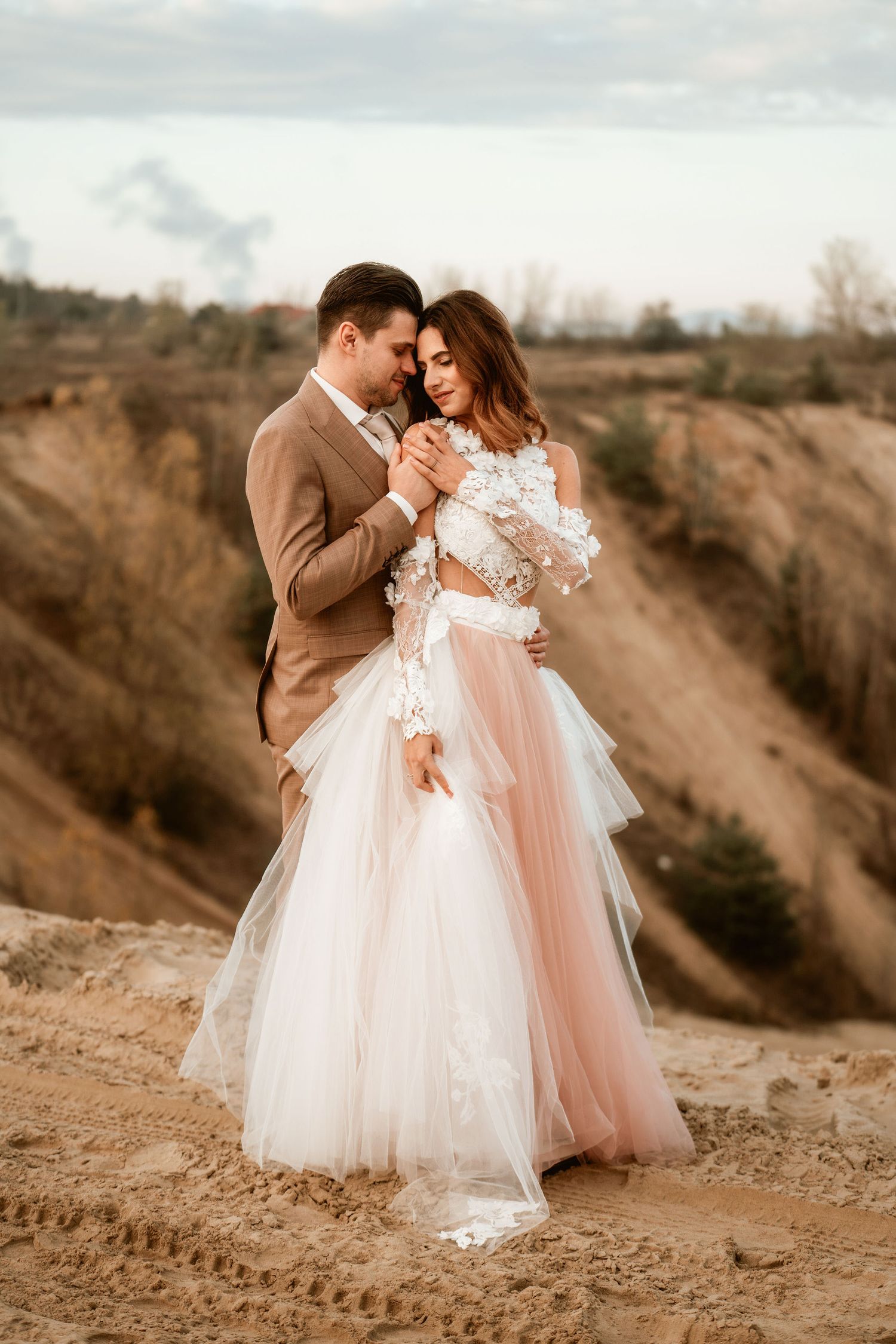A tender moment captured at a desert overlook with flowing blush wedding dress and tan suit.