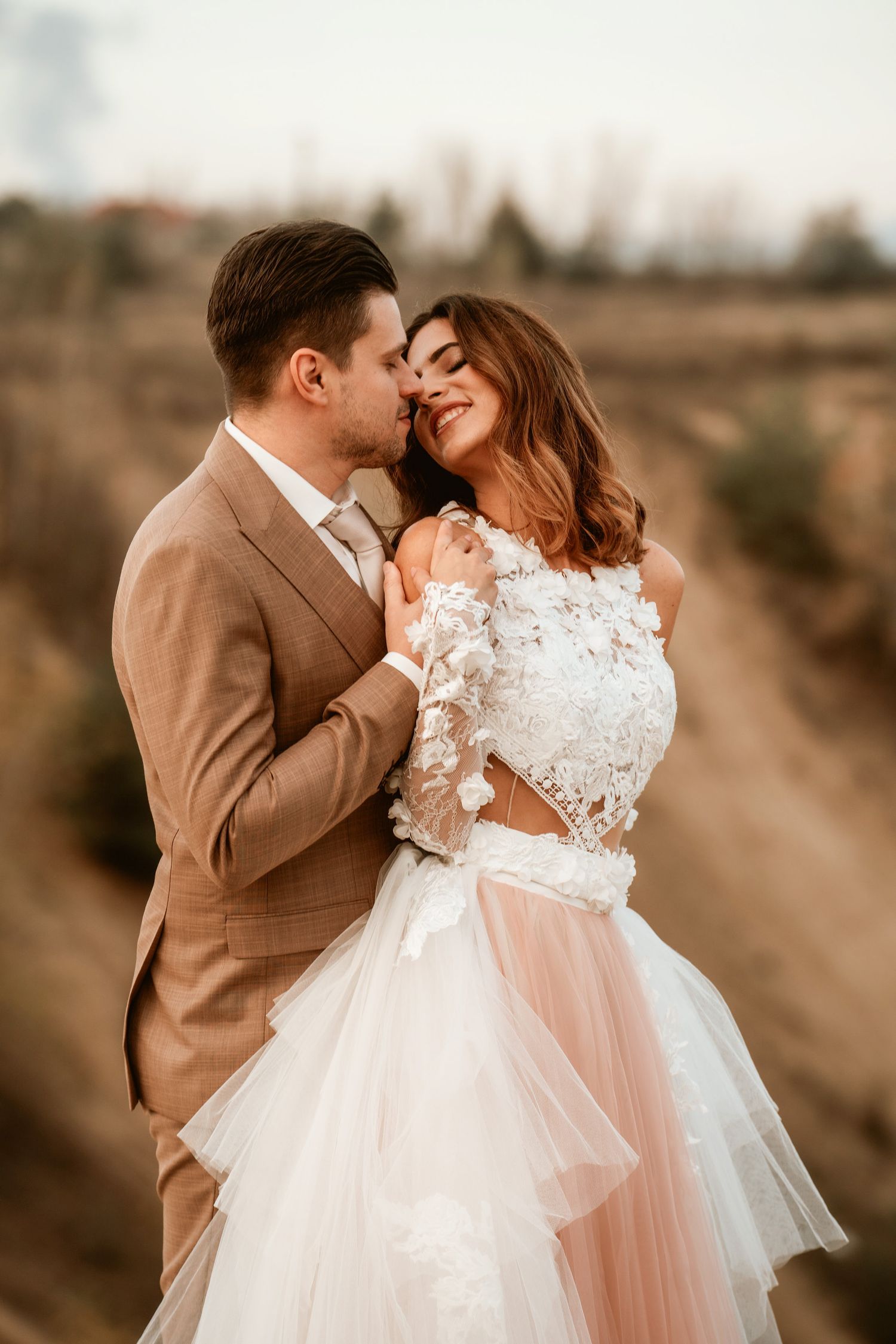 Intimate wedding portrait against dramatic desert landscape with elegant bridal gown details.