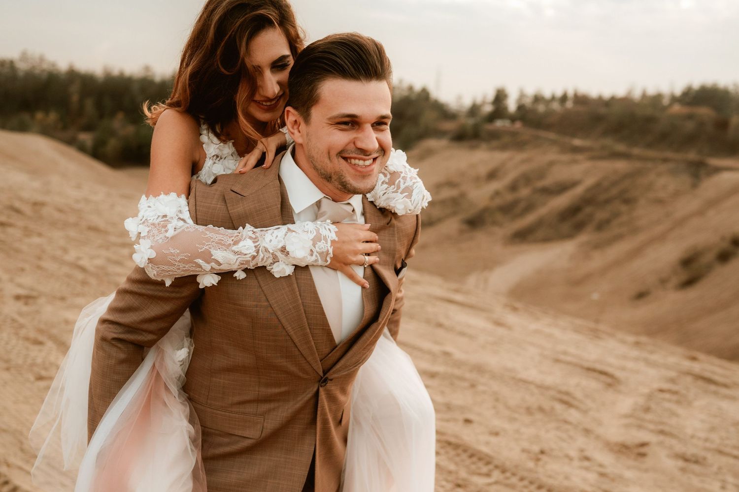 Candid piggyback ride moment during desert wedding photoshoot with blush and brown attire.