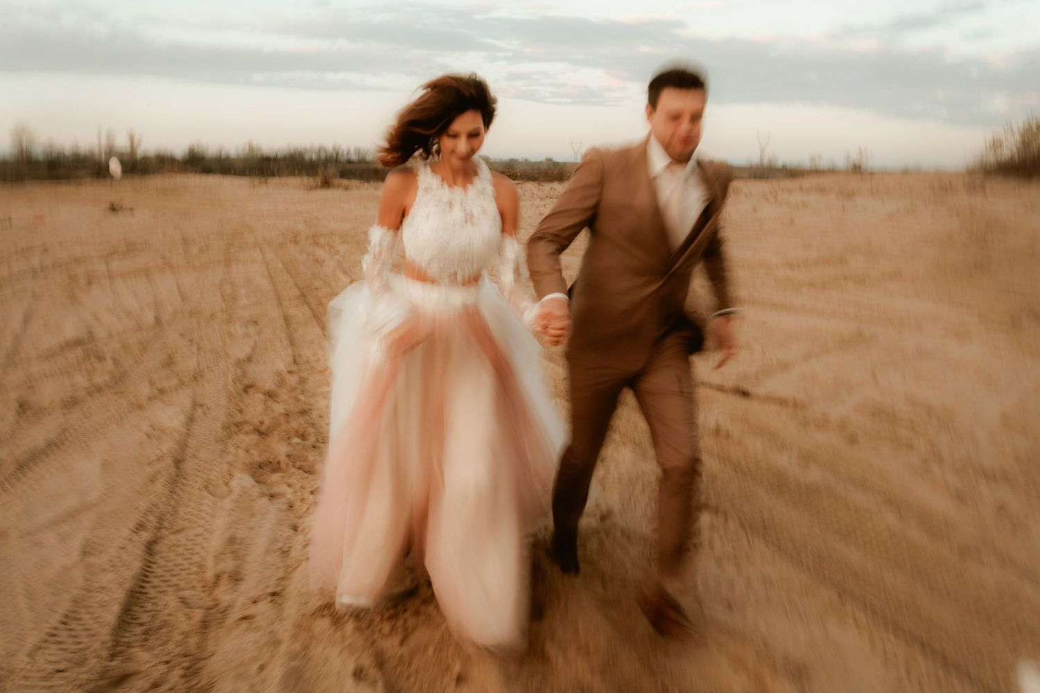 Motion-blur wedding photo capturing couple running through desert setting at dusk.