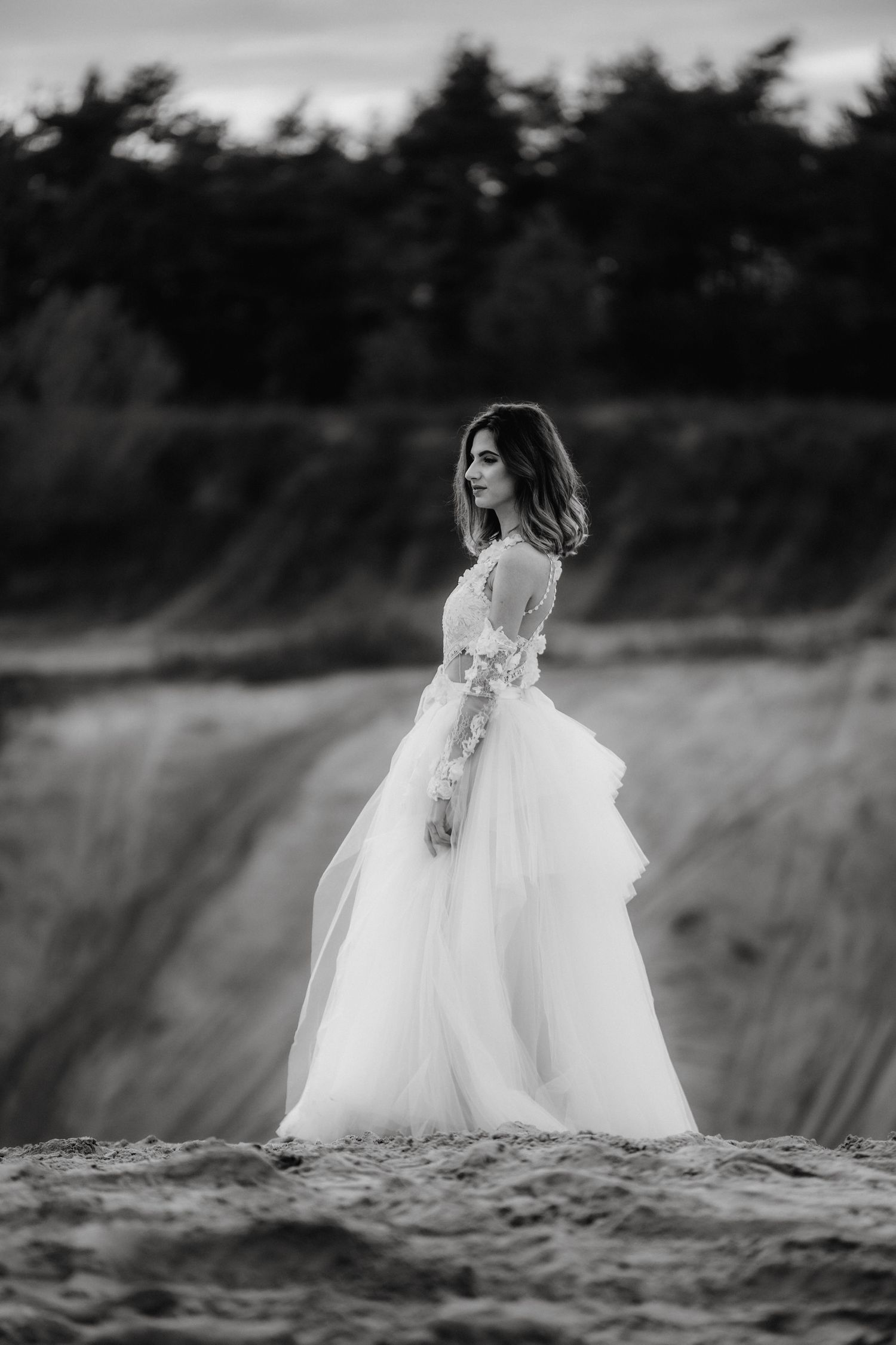 Black and white portrait of a bride in a layered tulle gown standing on rugged terrain.
