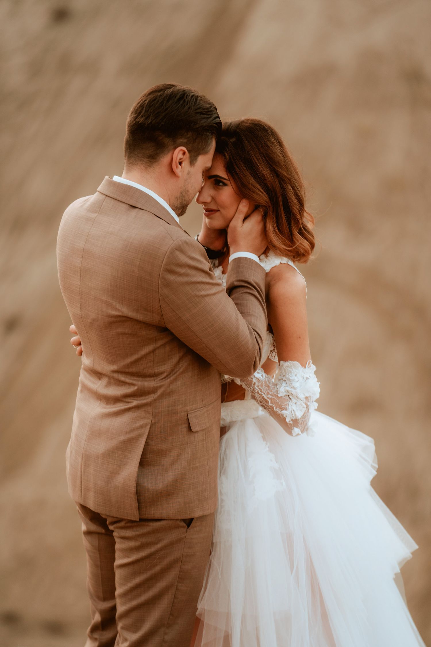 Romantic close-up of a couple embracing in wedding attire against an earthy backdrop.
