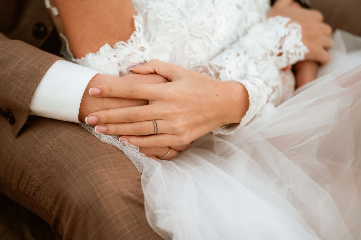 Close-up of wedding couple's hands with rings and white lace dress details.