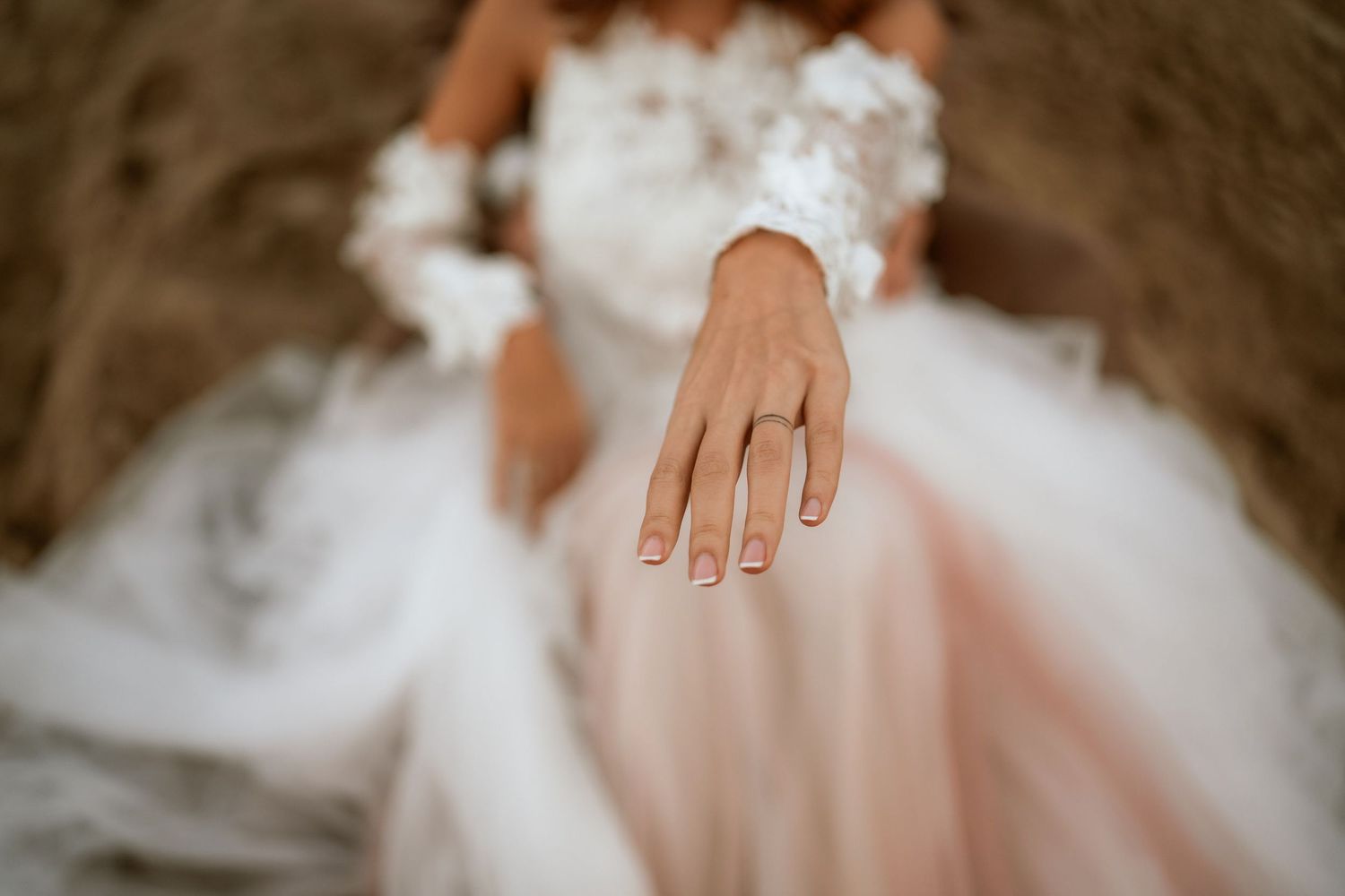 Close-up shot of wedding ring on bride's hand with white lace dress detail.