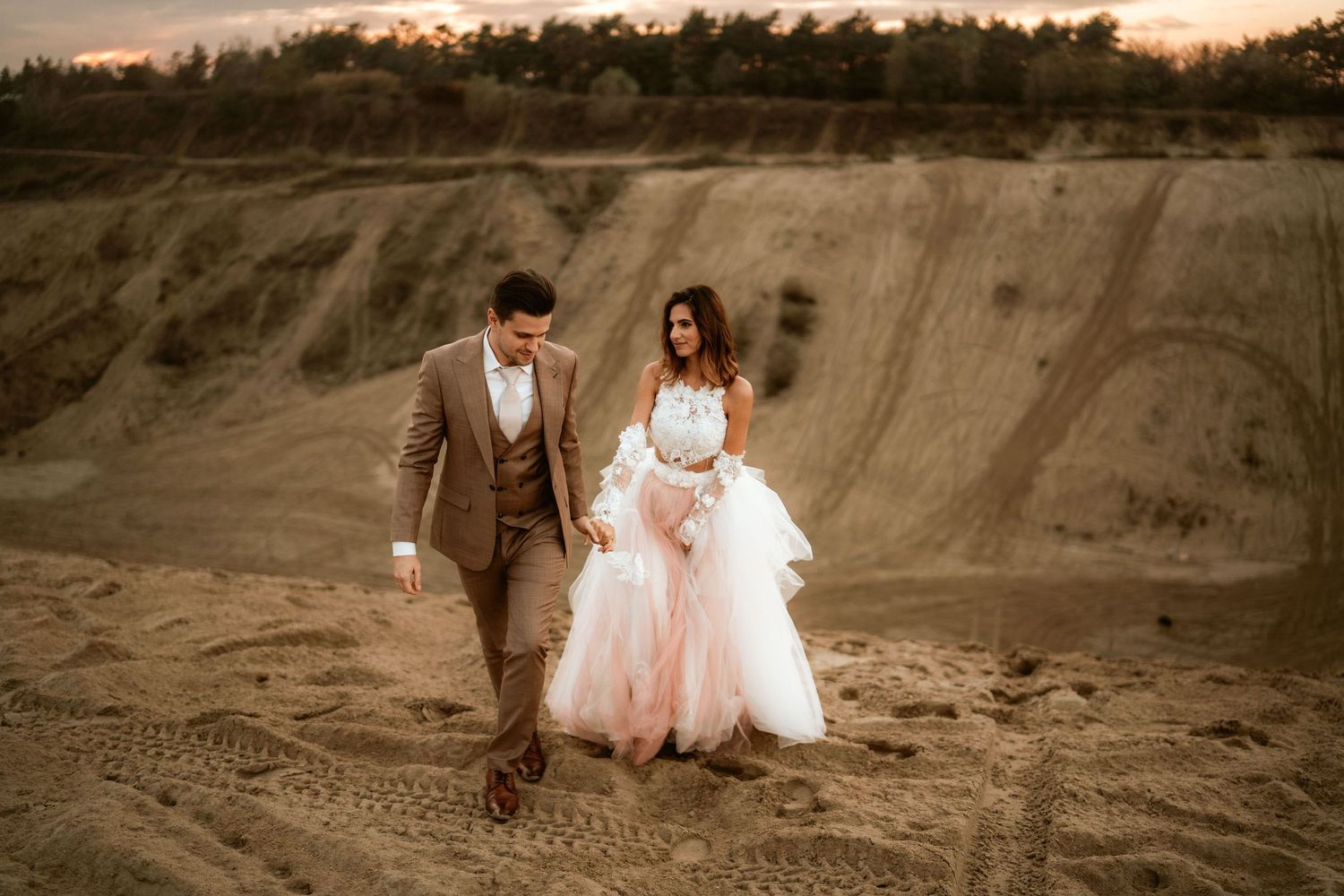 Newlyweds walking together on sandy terrain during sunset wedding photoshoot.