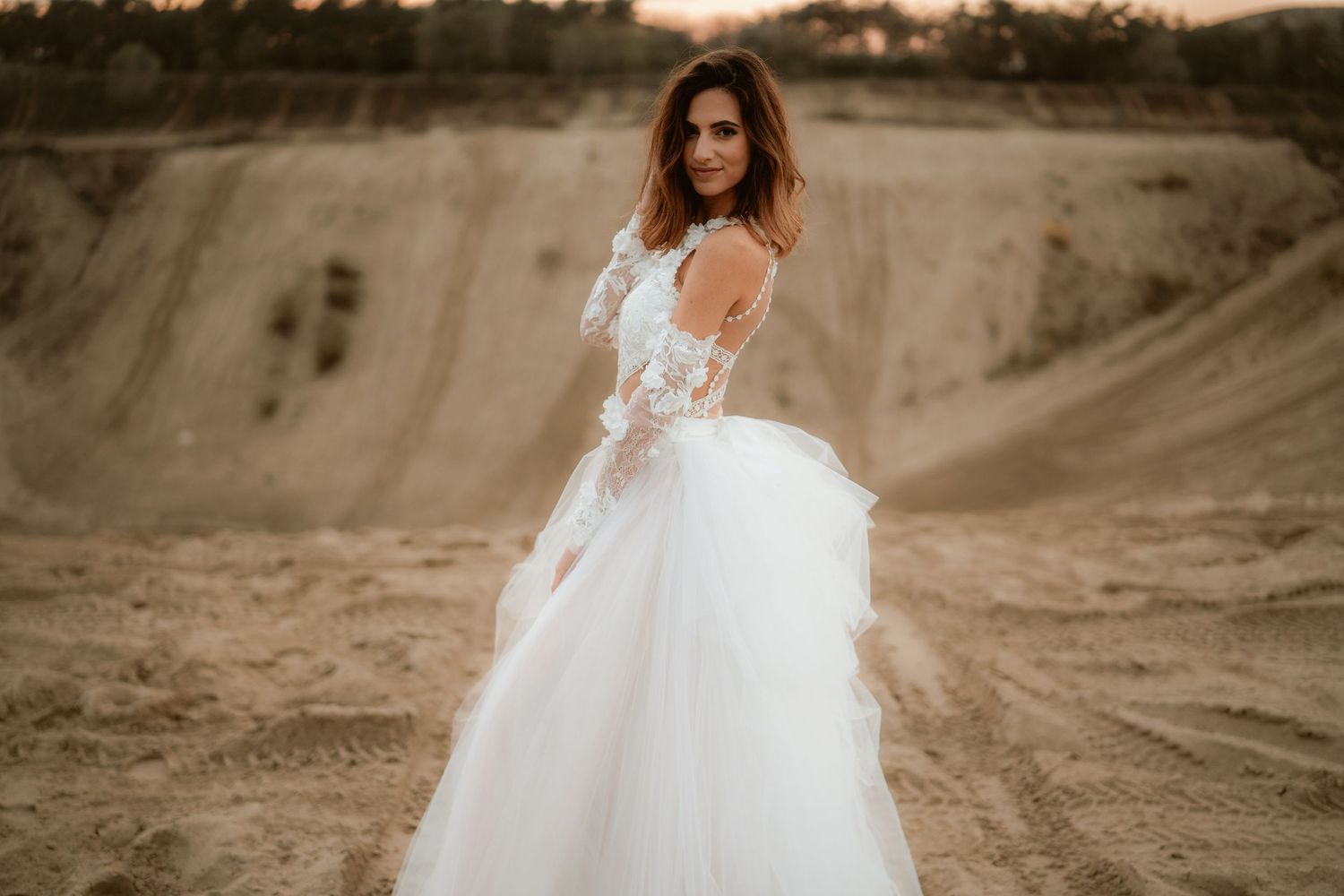 Bride in flowing white dress poses against dramatic quarry backdrop during golden hour.