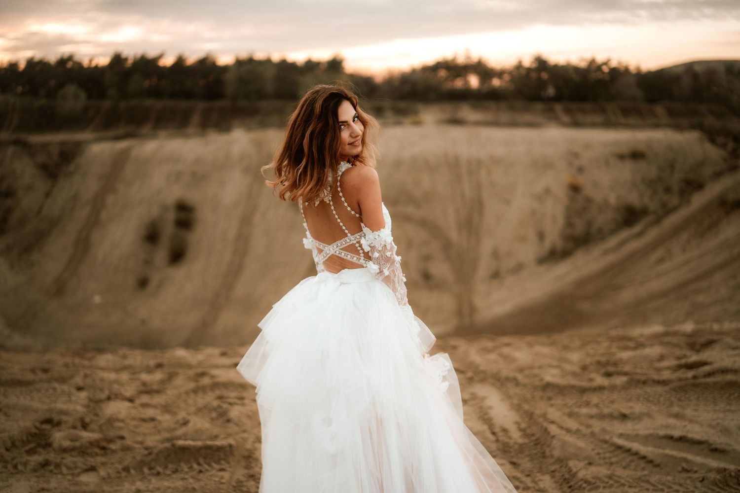 Bride in elegant backless wedding dress twirls against sunset desert landscape.