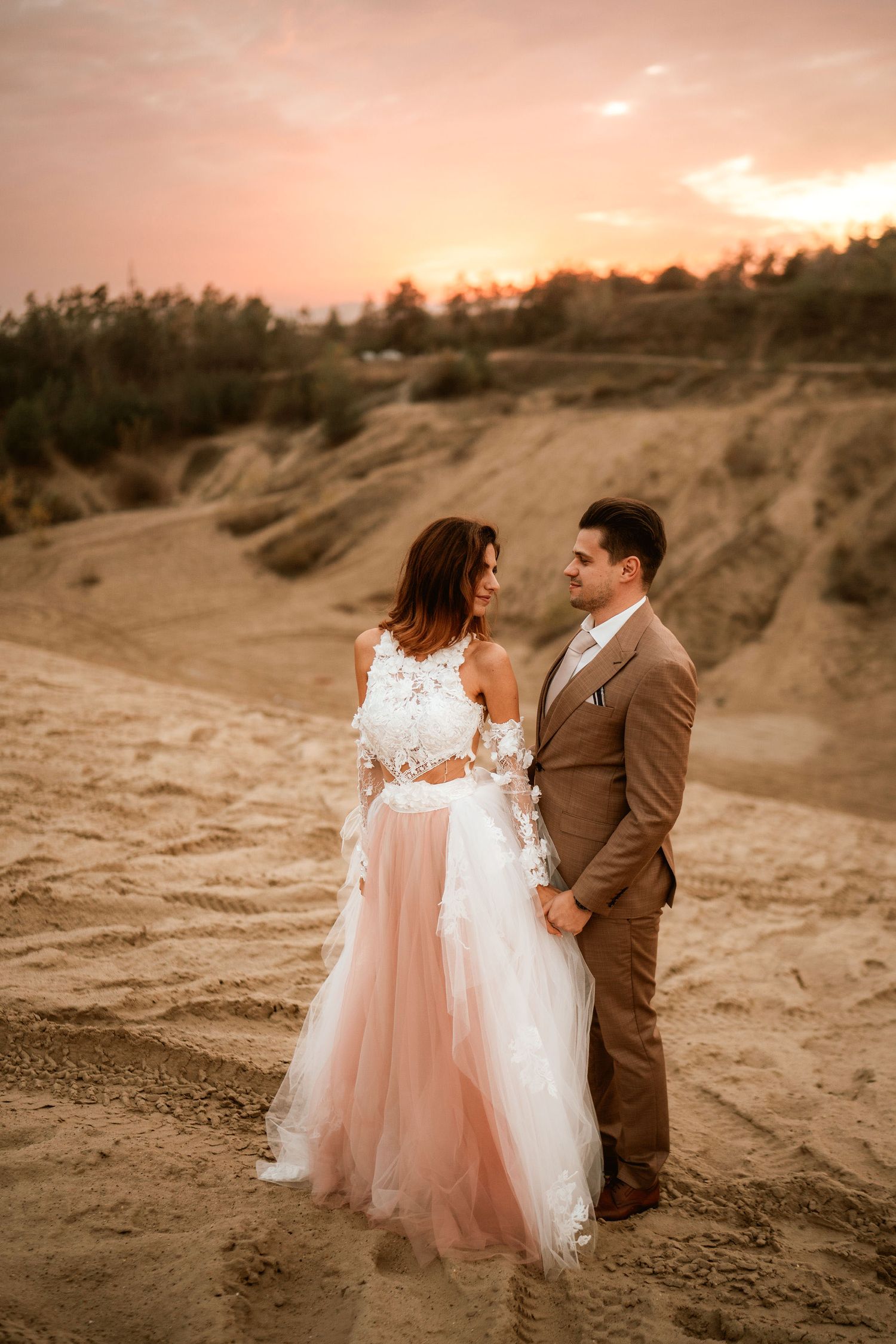 Couple in wedding attire embraces during golden hour in a desert landscape.