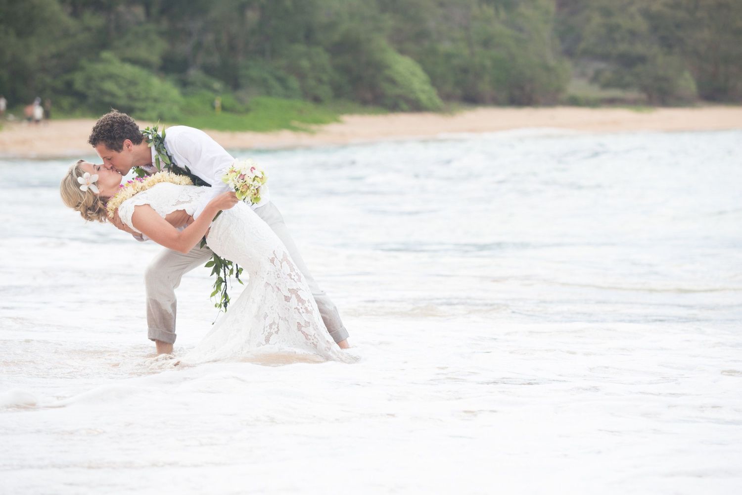 Romantic beachside wedding photo with couple embracing near the ocean waves.