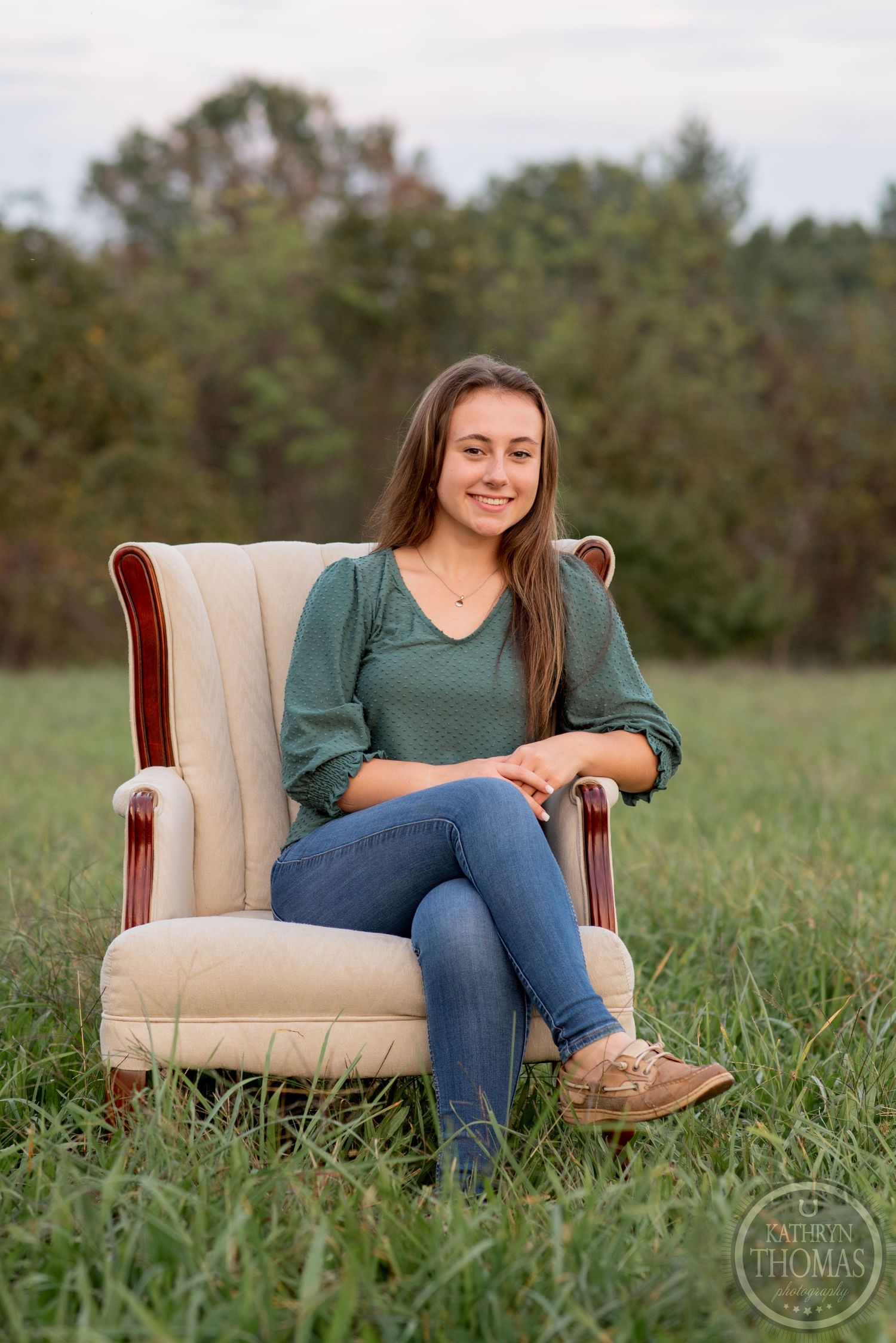 A relaxed outdoor portrait session with a vintage beige armchair placed in tall grass.