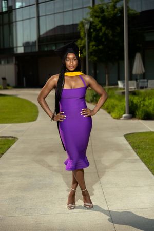 Graduate in a fitted purple dress and cap strikes confident poses on a campus sidewalk.