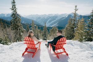 Red chairs positioned on snowy overlook with mountain range backdrop.