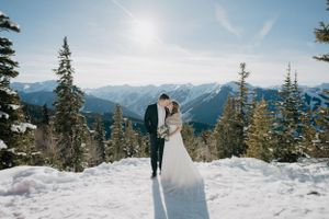 Newlyweds sharing moment against snowy mountain landscape on sunny winter day.