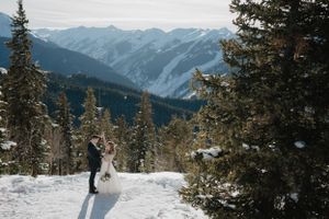 A wedding couple poses against a dramatic mountain backdrop in winter with snow-covered peaks.