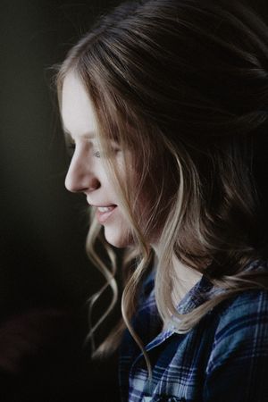 Side profile portrait of a young woman with wavy hair wearing a plaid shirt in moody lighting.