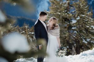 A couple shares an intimate moment in a winter mountain setting with snow-covered trees.