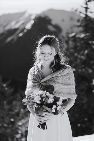 A black and white portrait of a bride holding a bouquet with mountains in the background.