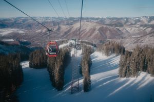 Scenic view of ski gondolas ascending over snow-covered terrain with mountain peaks in the background.