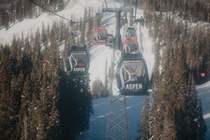 Multiple ski gondolas traverse snow-covered slopes at Aspen Mountain resort with evergreen trees in winter.