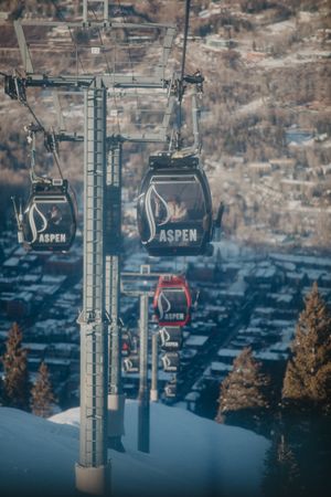 Aspen ski resort gondolas suspended against a winter mountain landscape with snow-covered slopes below.