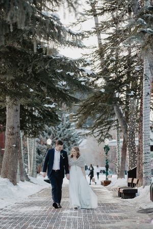 A couple walks along a snow-covered path lined with illuminated trees in a winter wonderland setting.