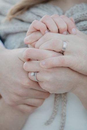 Close-up of clasped hands wearing silver wedding bands against a light fabric background.