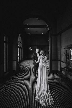 Black and white wedding photo of a couple in a grand hallway with dramatic lighting.