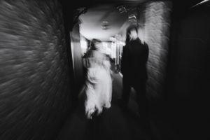 Artistic motion blur photo of wedding couple walking through dark corridor.